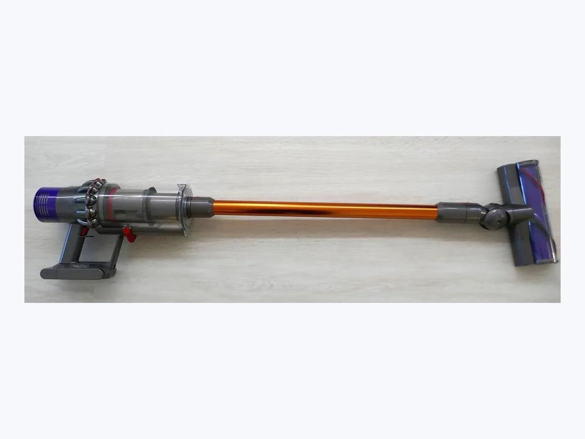 Dyson Cyclone V10 Absolute cordless stick vacuum with orange wand and motorised cleaner head, top-down view on a light floor