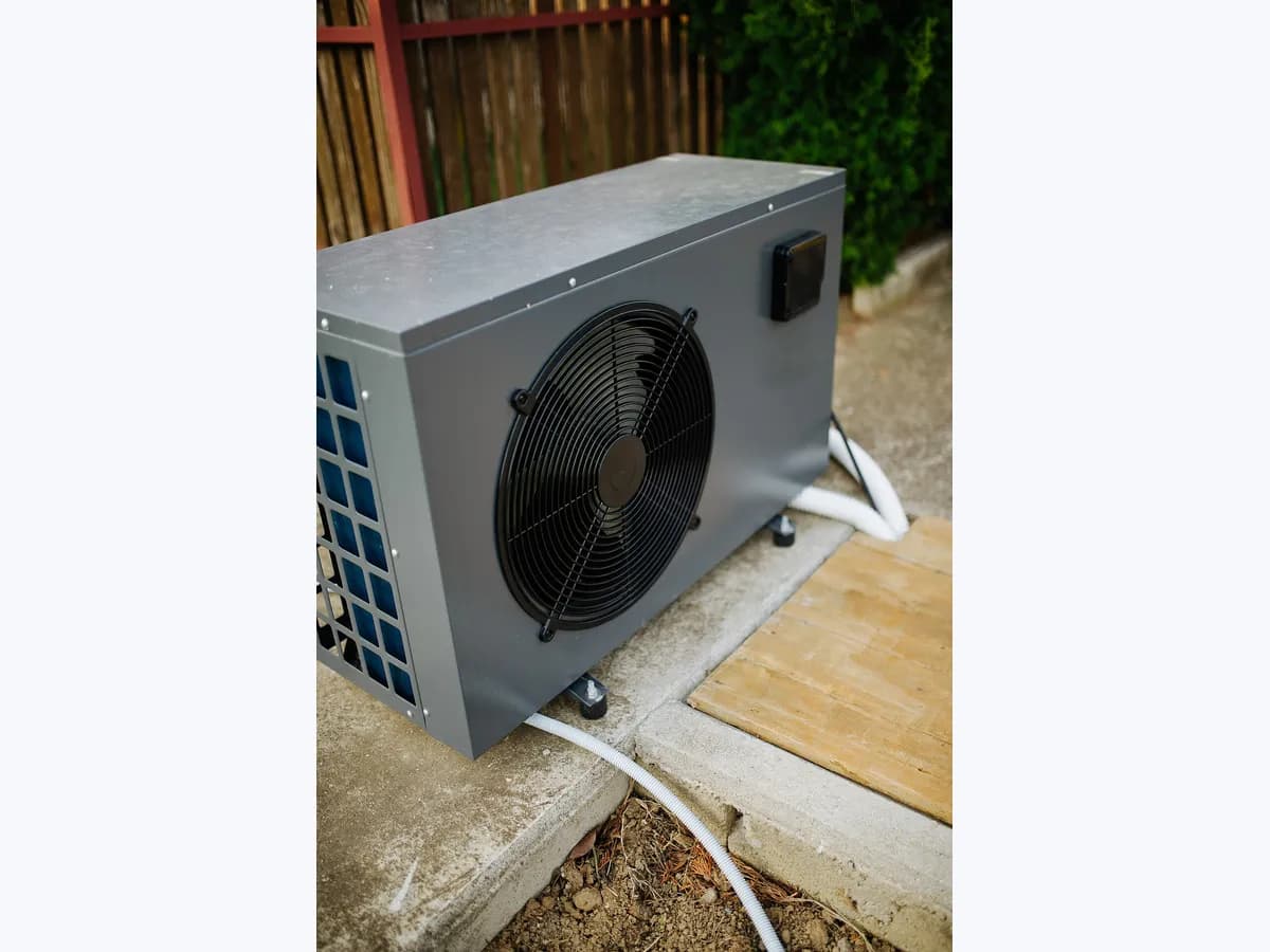 Pool heat pump with front fan and water hoses installed in a garden