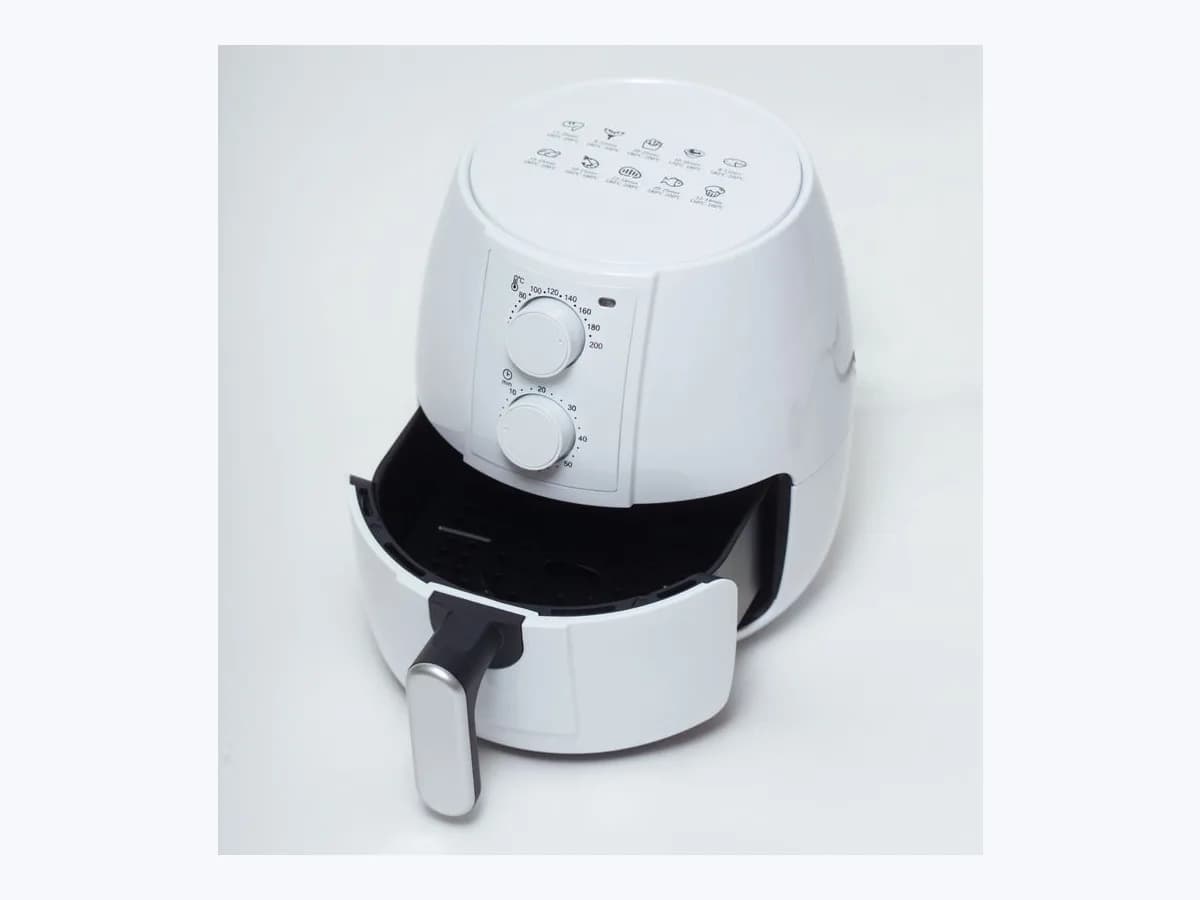 White countertop basket-style air fryer with temperature and timer dials and the removable basket partially open.