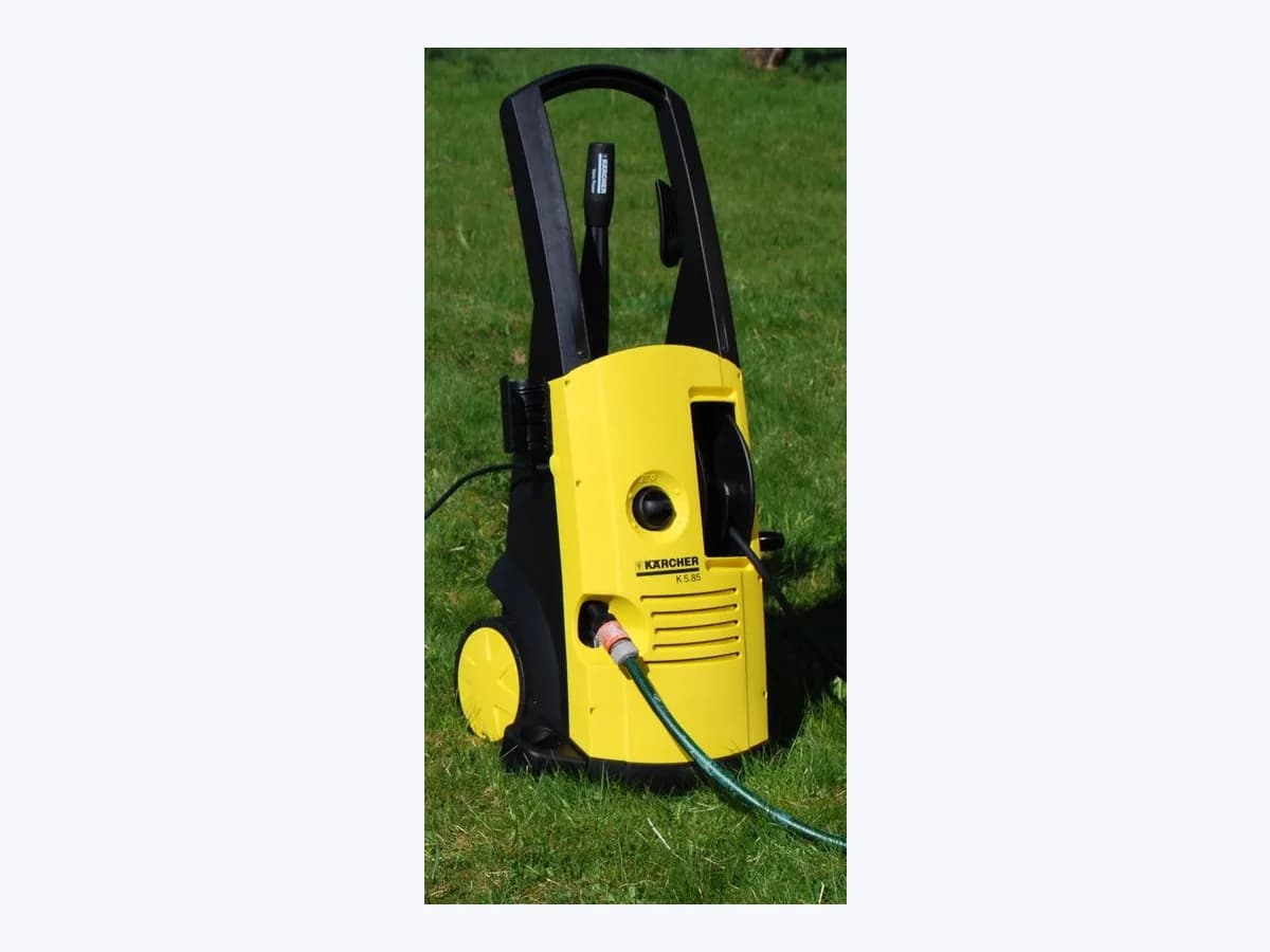 Yellow and black Kärcher K 5.85 wheeled pressure washer with the spray lance stored in the handle and a water hose connected