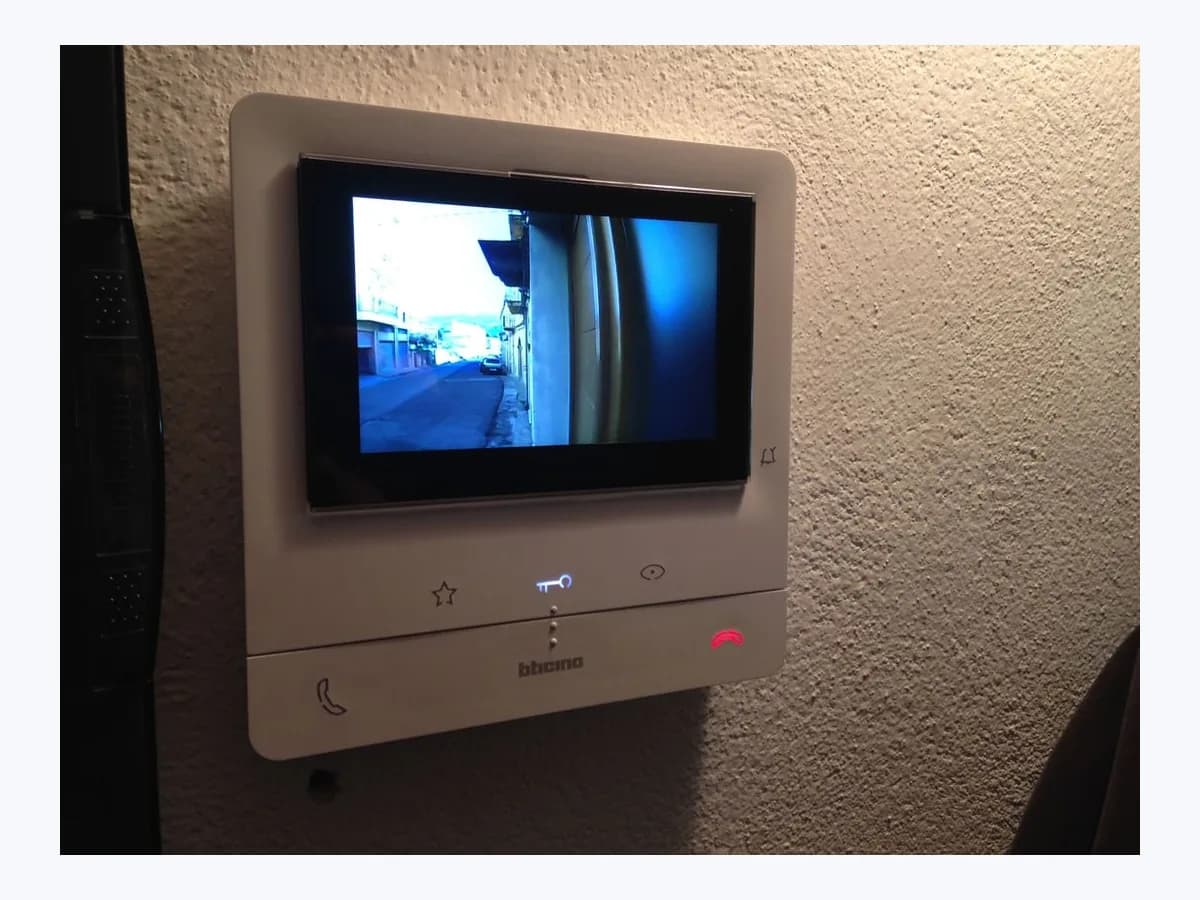 Wall-mounted white Bticino indoor video door intercom monitor with an active 5-inch color screen and illuminated touch buttons for door unlock and call control