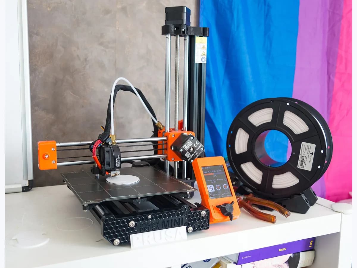 Original Prusa MINI filament 3D printer next to a spool of white filament